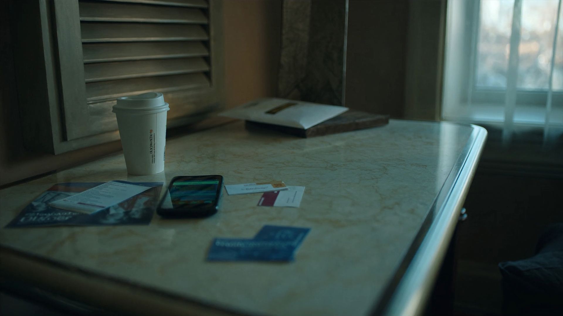 A motel table in morning light with a phone, business cards, flyers, and an envelope.