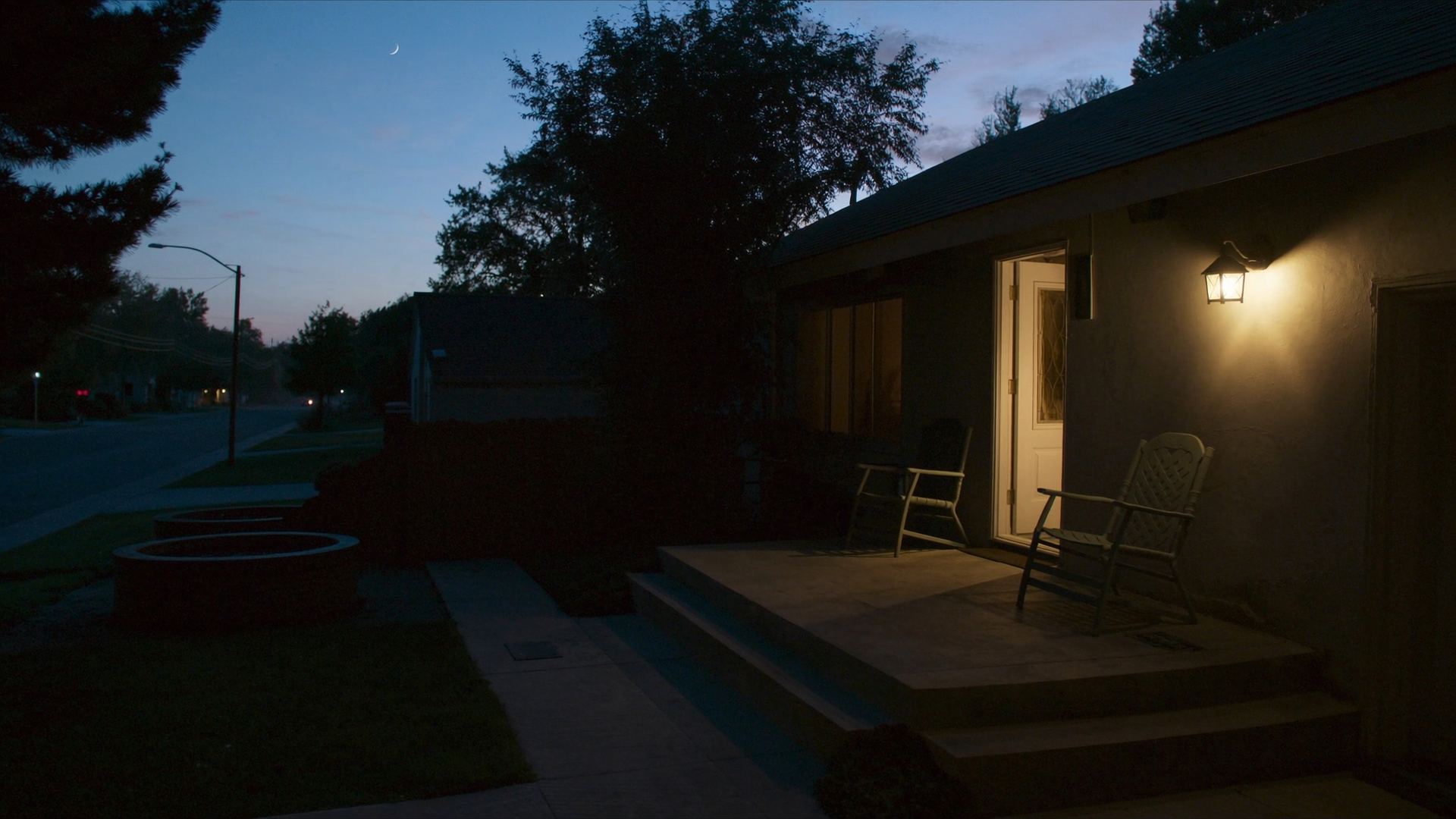 A front porch at dusk with the light on and two empty chairs.
